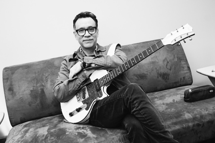 Fred Armisen sitting on a sofa with a guitar